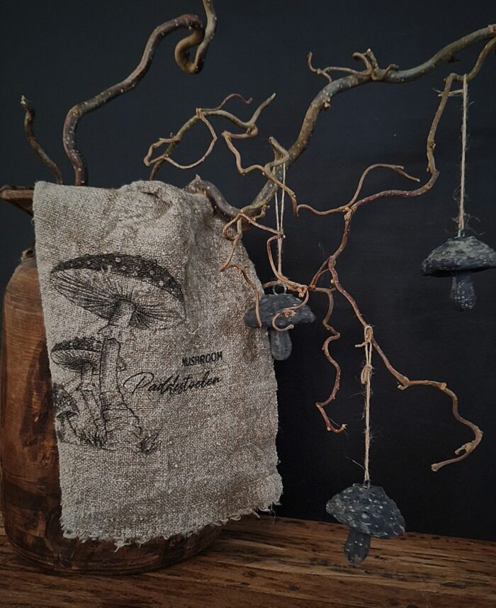 linnen shabby doek met paddenstoelen, geplaatst op een Nepalese kruik met takken, daaraan hangende Brynxz paddenstoelen