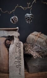 Shabby kerstlint met tekst frohe weihnachten, geknoopt aan een nepalese kruik, gecombineerd met een oude houten poer, tijmkrans en dennenappels