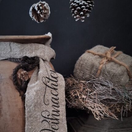 Shabby kerstlint met tekst frohe weihnachten, geknoopt aan een nepalese kruik, gecombineerd met een oude houten poer, tijmkrans en dennenappels
