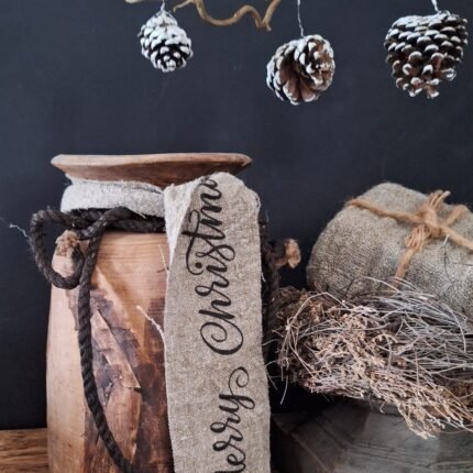 Shabby kerst lint met tekst Merry Christmas om een Nepalese pot, gecombineerd met een houten poer, tijmkrans en dennenappels