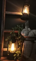 Zwart metalen stormlantaarn op stroom, hangend aan een ladder. gedecoreerd met een houten kruik en linnen pompoen