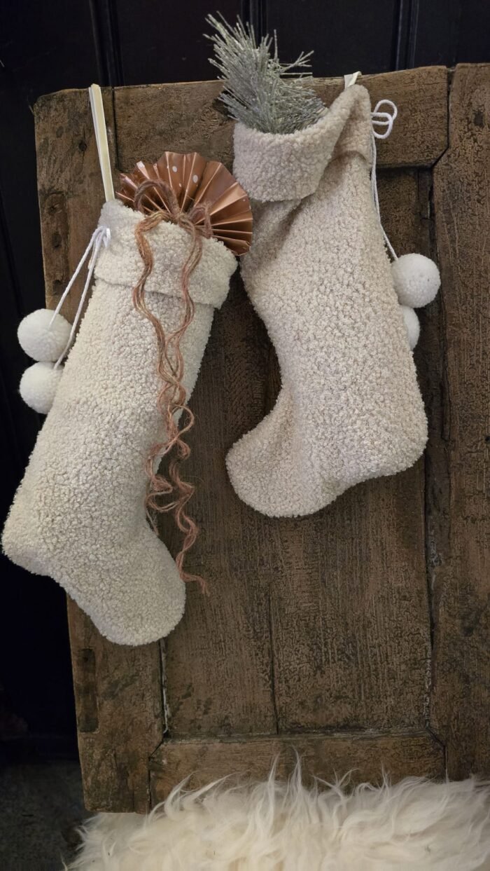 Kerstsok Ellabritt S crème gevuld met cadeau en dennentak aan een oude houten deur