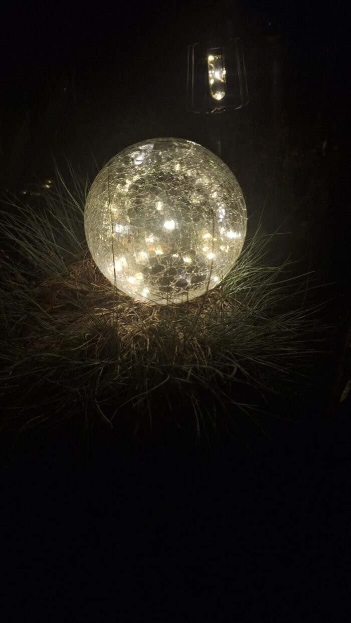 Glazen lichtbol met warm LED-licht in tuin bij nacht