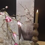 Landelijk wandbord met afbeelding van kruik en magnolia tak, decoratief met witte vaas en houten kandelaar met kaars, sfeervolle landelijke woondecoratie.